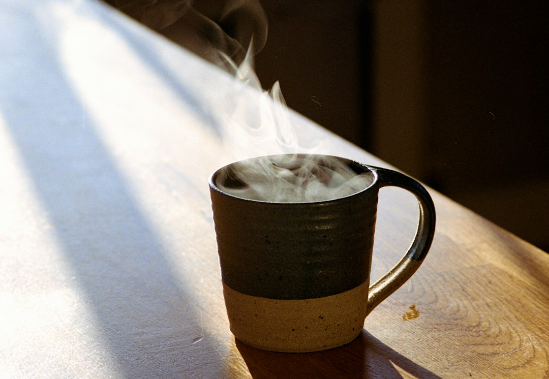 Taza de cerámica con bebida humeante sobre mesa de madera iluminada por luz natural