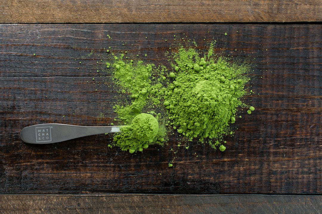 Cucharilla gris con polvo de matcha verde brillante esparcido sobre tabla de madera oscura