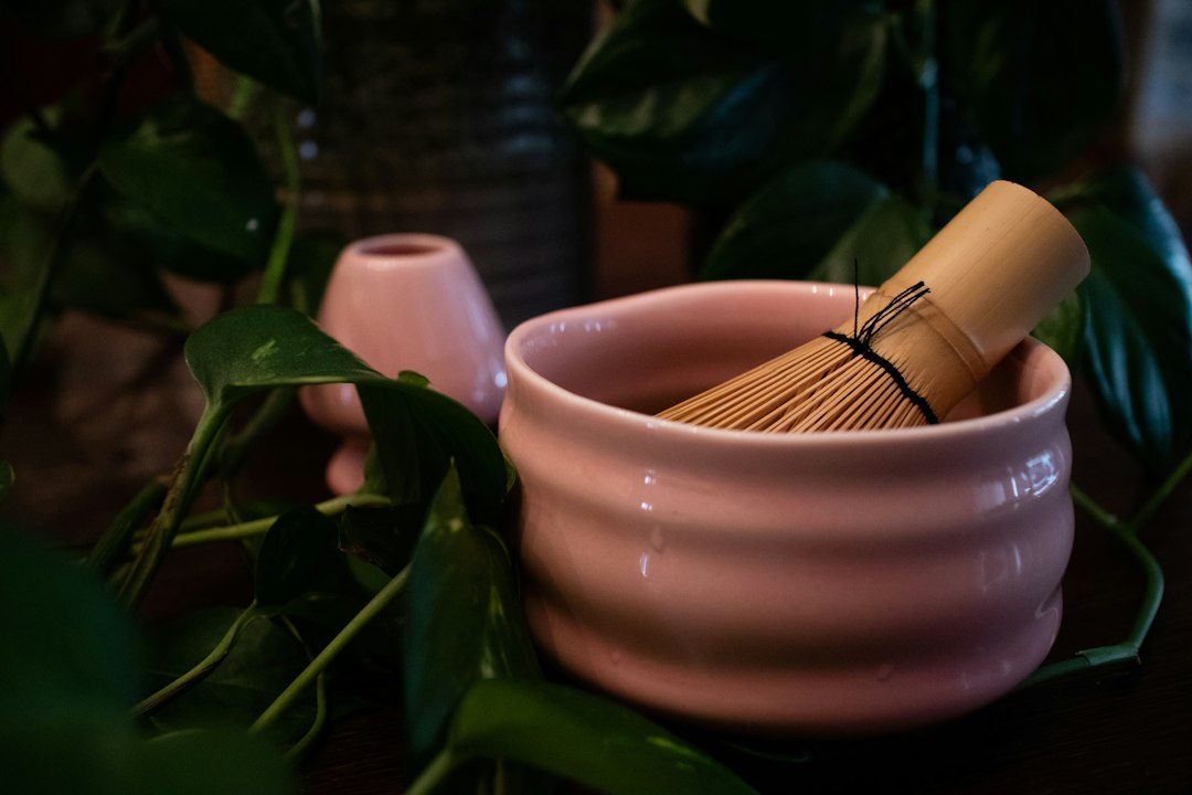 Cuenco de cerámica rosa con batidor de bambú para matcha ceremonial rodeado de plantas verdes