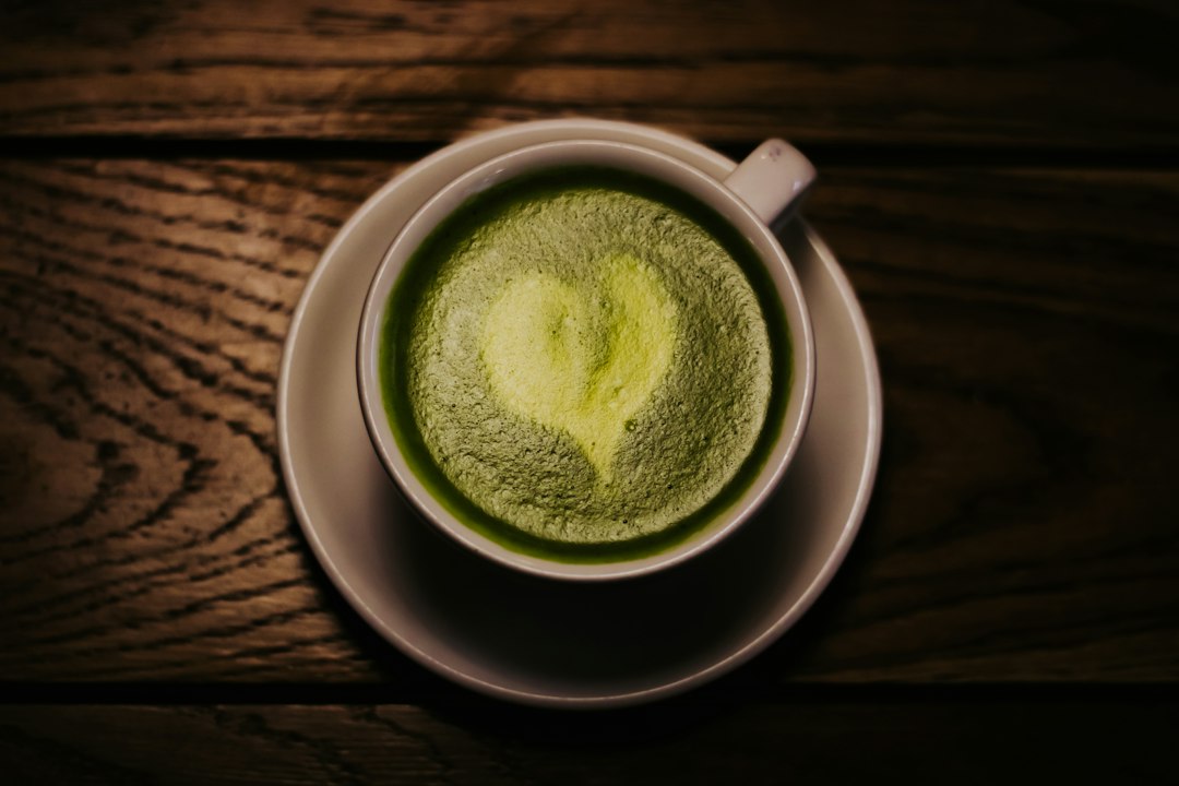 Taza de matcha latte con polvo verde matcha ceremonial disuelto en agua caliente sobre superficie de madera oscura