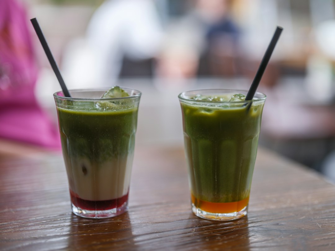 Dos vasos con recetas frías de matcha ceremonial, uno con capa roja en la base y otro con capa naranja, sobre mesa de madera