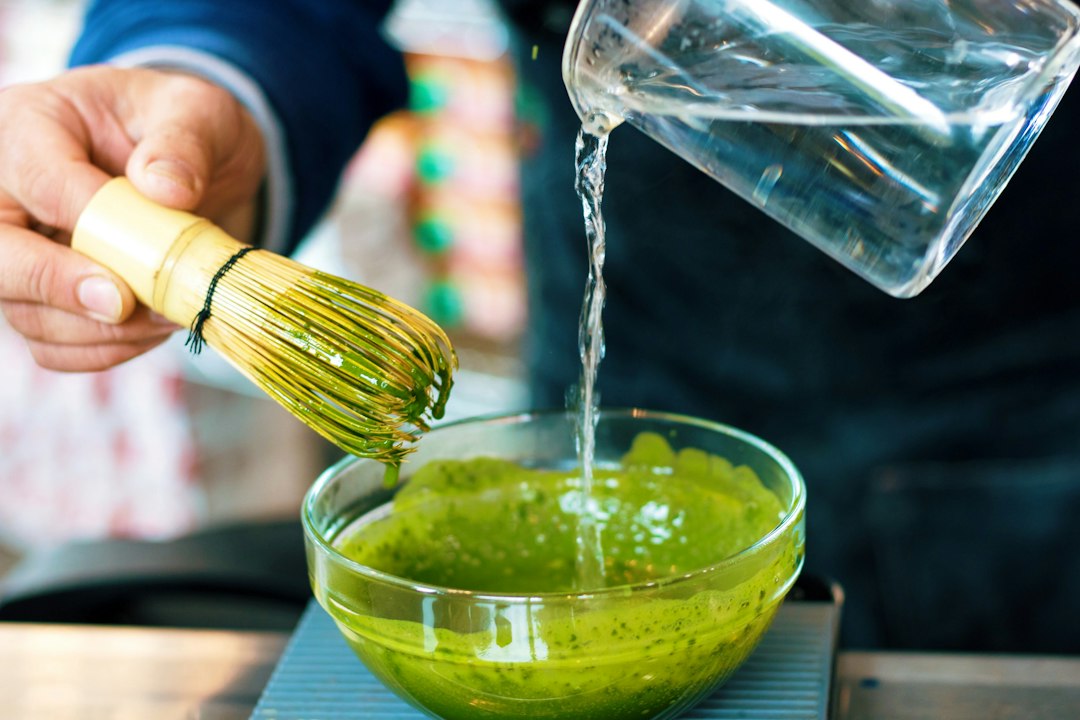 Preparación de matcha ceremonial con batidor de bambú vertiendo agua caliente en un bol con polvo verde