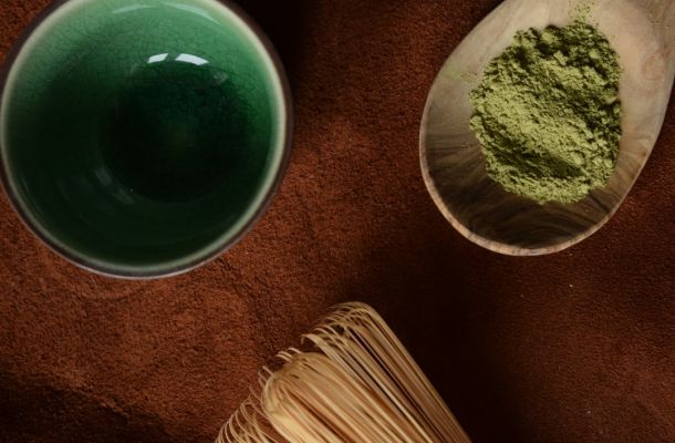 Preparación de matcha ceremonial con polvo verde, recipiente de cerámica y utensilio tradicional de bambú en superficie