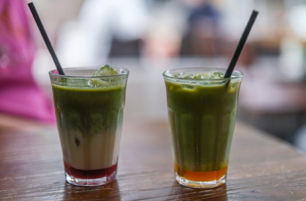 Bebidas frías de matcha verde con capas de colores contrastantes y pajitas negras en vasos de vidrio sobre mostrador