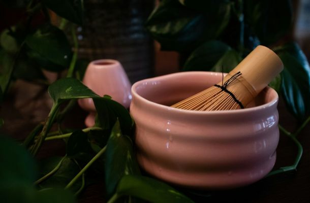 Utensilios matcha ceremonial: cuenco rosa y batidor de bambú en ambiente con vegetación