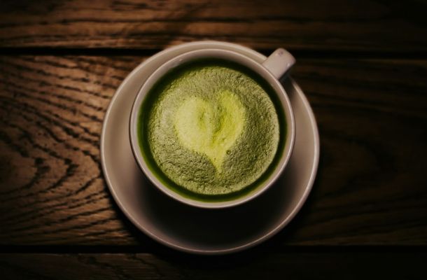 Taza de matcha latte con polvo verde matcha ceremonial disuelto en agua caliente sobre superficie de madera oscura