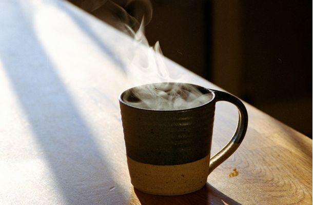 Taza de cerámica con bebida humeante sobre mesa de madera iluminada por luz natural